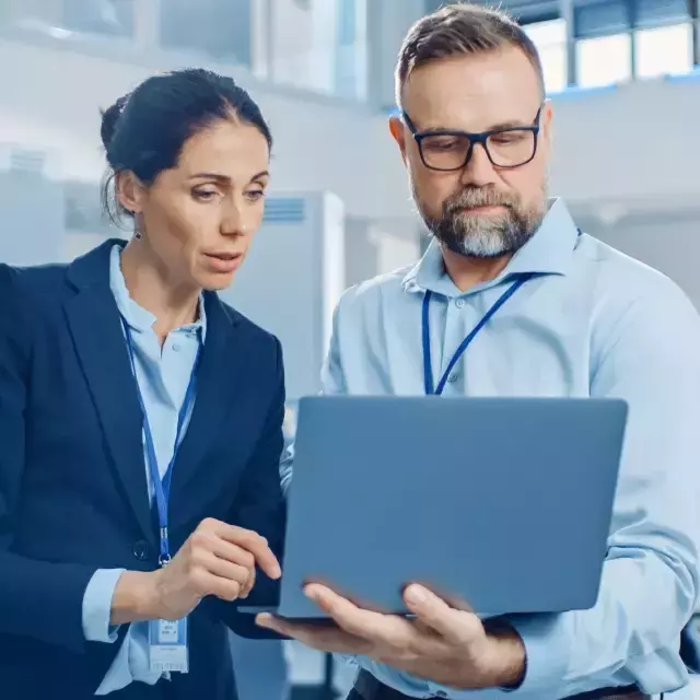 Businessman and woman collaborating over a laptop in an office, discussing contract management strategies and risks.