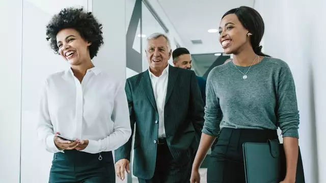 A diverse group of smiling business professionals walking through a modern office hallway together.