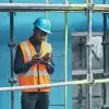 Construction worker in a hard hat and vest checking his phone on a scaffold.