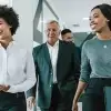 A diverse group of smiling business professionals walking through a modern office hallway together.